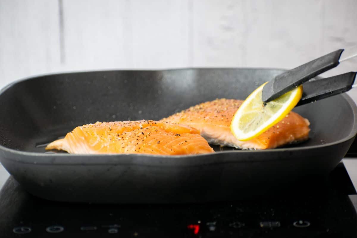 How to Cook Salmon With Skin Step 5 2 salmon fillets in pan with a lemon slice.