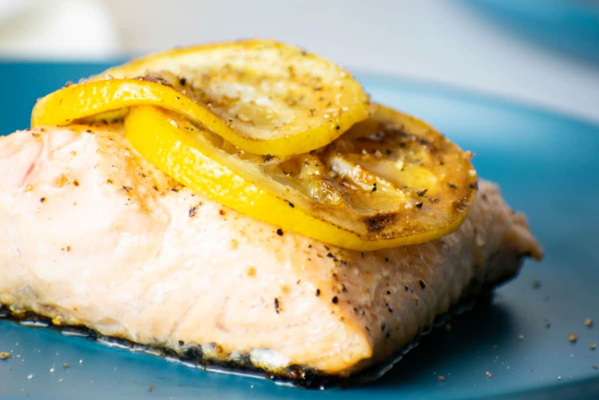 Cooked salmon fillet with lemon slices on blue plate.