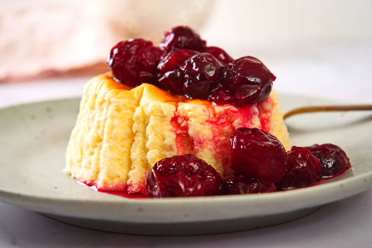 Cherries in syrup over cake on plate.