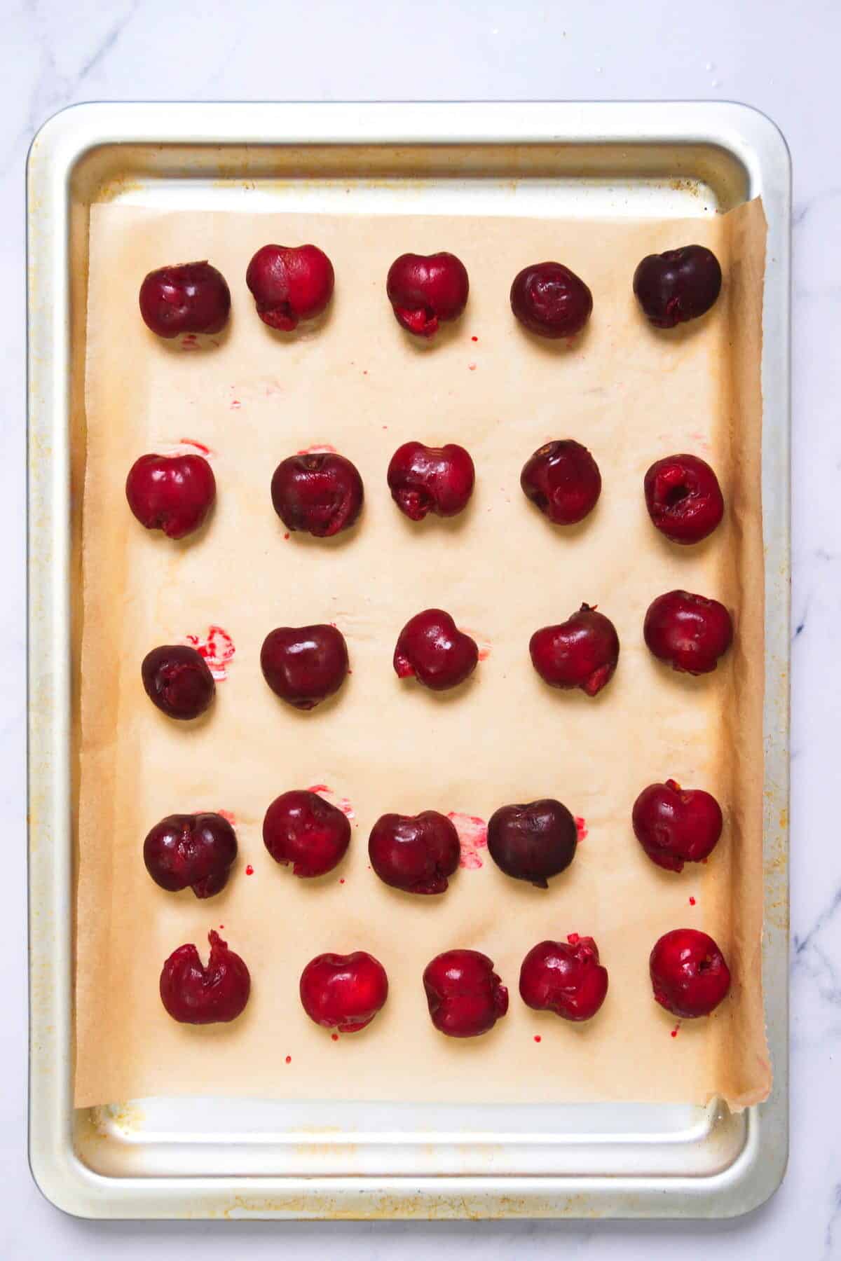 Pitted cherries on pan, spaced apart.