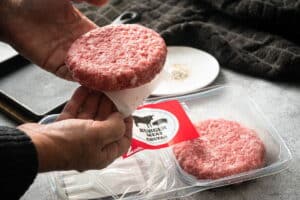 Raw burger patties in a package with paper separators.