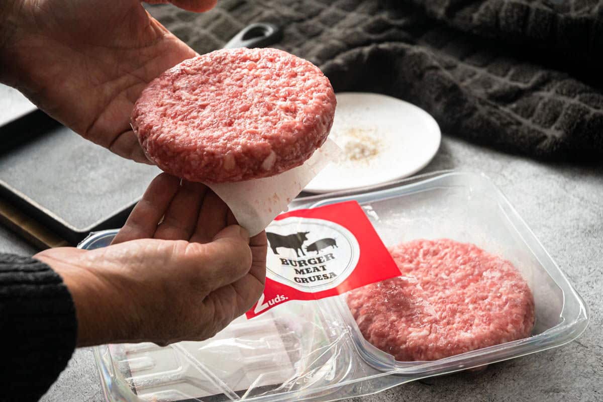 Raw frozen burger patties in a package with paper separators.