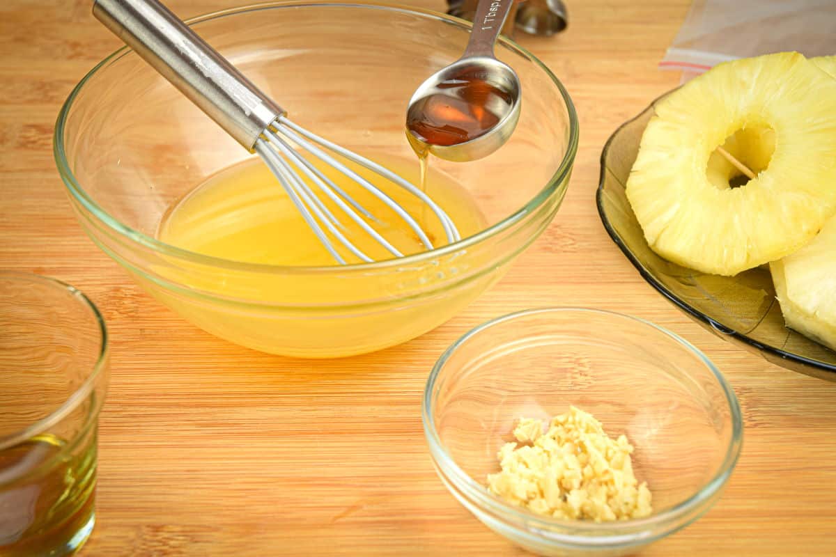 How to Grill Pineapple Slices_2 Orange juice marinade in a small glass bowl with minced garlic and pineapple slices on the side.