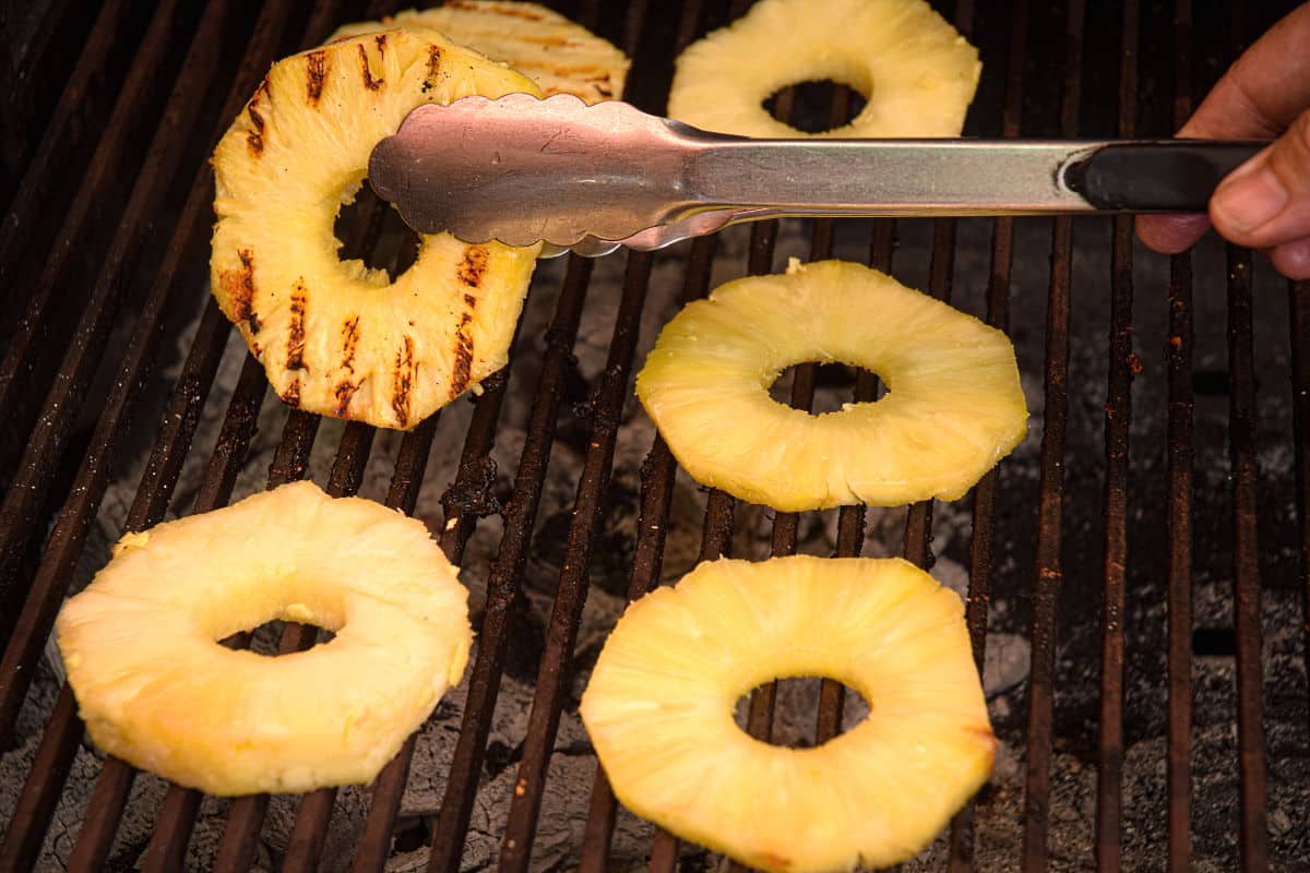 How to Grill Pineapple Slices_9 Pineapple slices on the grill with tongs.