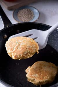 Kimchi pancakes in a frying pan with a flipper.