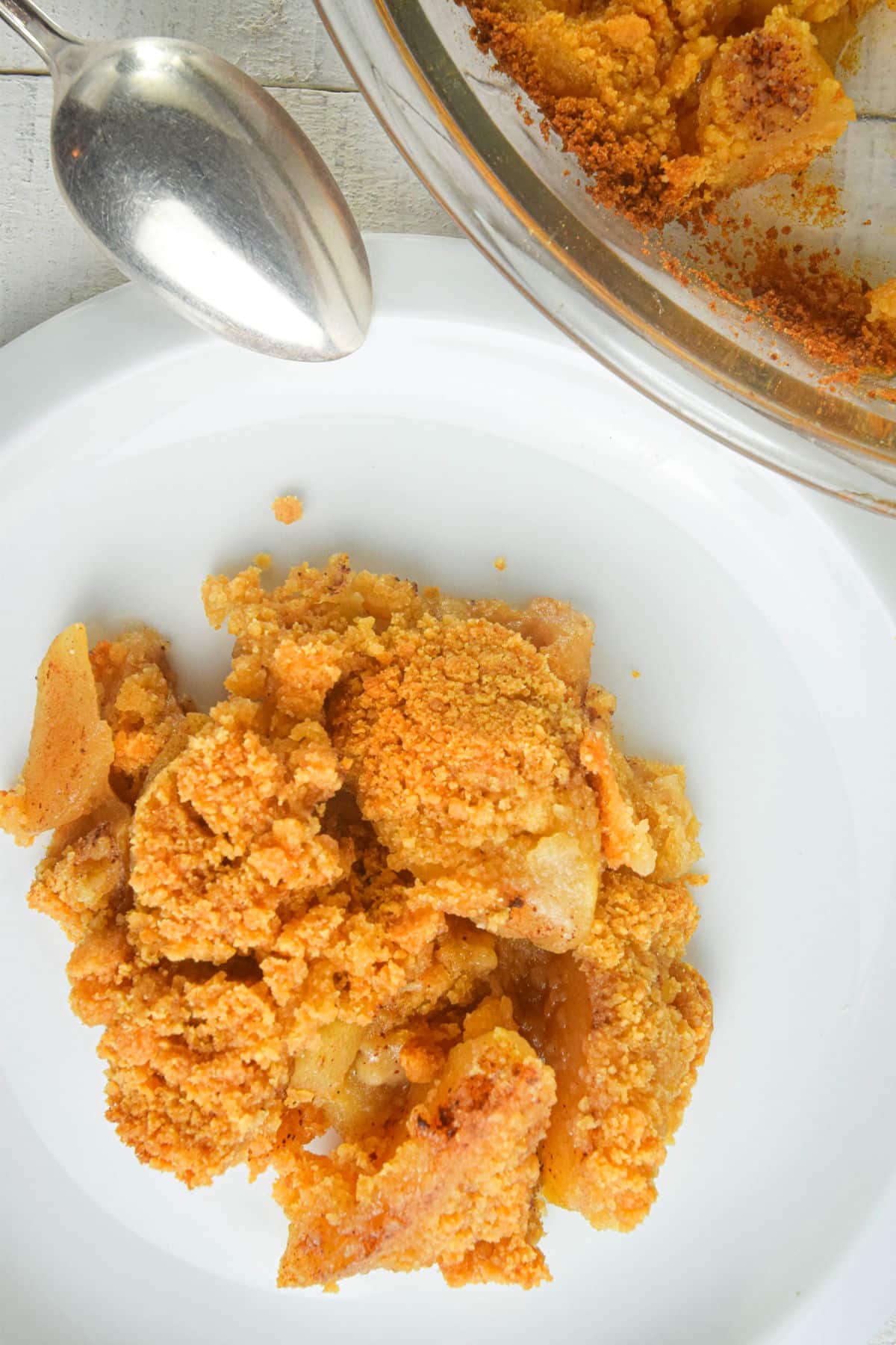 Apple crisp on white dessert plate with a spoon on the side.