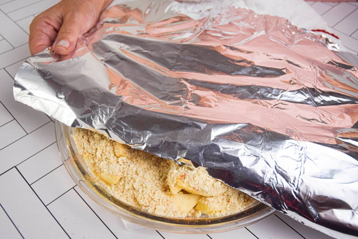 Unbaked apple crisp in a pie dish with foil on top.