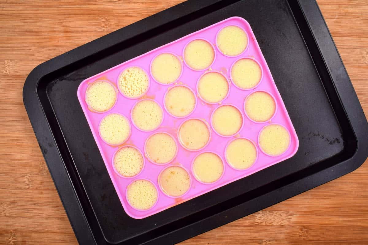 How to Make Cake Pops with a Mold Step 6-3 Cake pop mold with batter in it on sheet pan, wooden background.