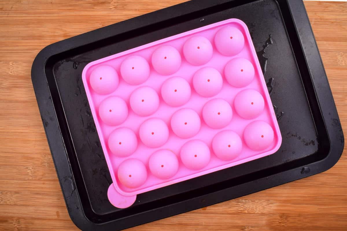 How to Make Cake Pops with a Mold Step 6-4 Pink cake pop mold on sheet pan, wooden background.