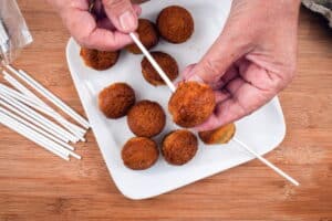 Bare cake pops on white plate, wooden background.