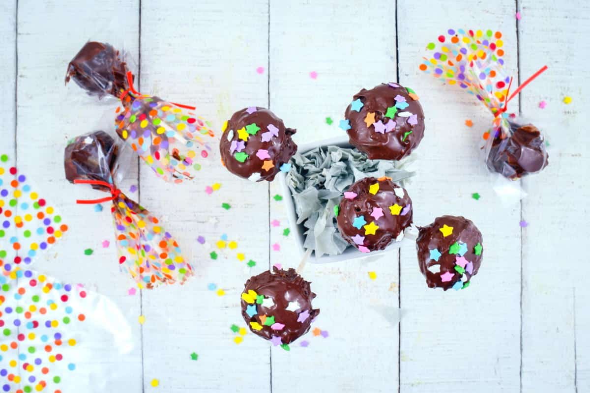 How to Make Cake Pops with a Mold 5 Chocolate cake pops with sprinkles, wrapped in cellophane, on white wooden background.