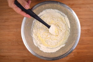 Cake pop batter and spatula in metal bowl, wooden background.