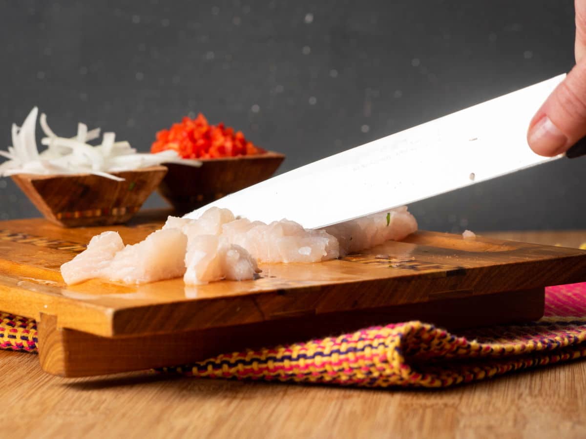 How to Make Ceviche - Step 3 Cubed raw white fish on cutting board with knife.