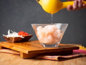 Glass bowl with raw white fish and a lemon juicer.