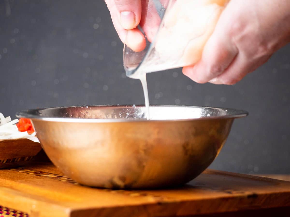 How to Make Ceviche - Step 6 Metal bowl and glass bowl with lemon juice pouring out.