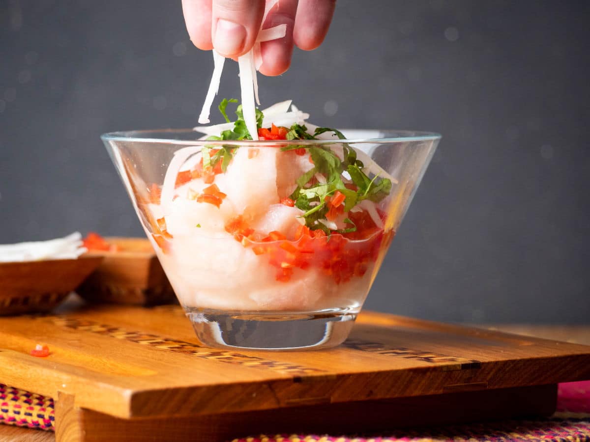 How to Make Ceviche - Step 7 Ceviche in a glass bowl with onion, cilantro and red chili peppers.