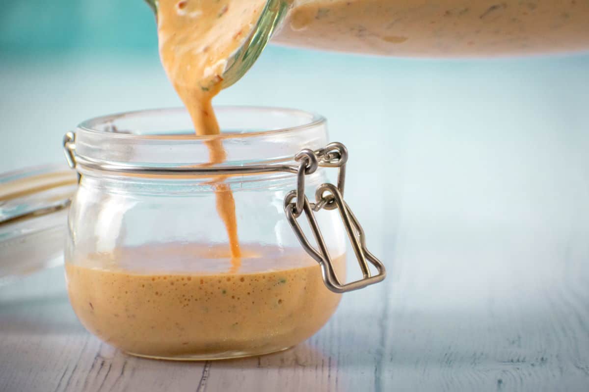 How to make chipotle sauce Step 3 Chipotle sauce pouring into a jar on blue background.