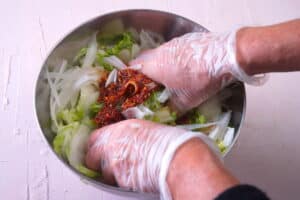 Hands massaging cabbage and spices in a steel bowl.