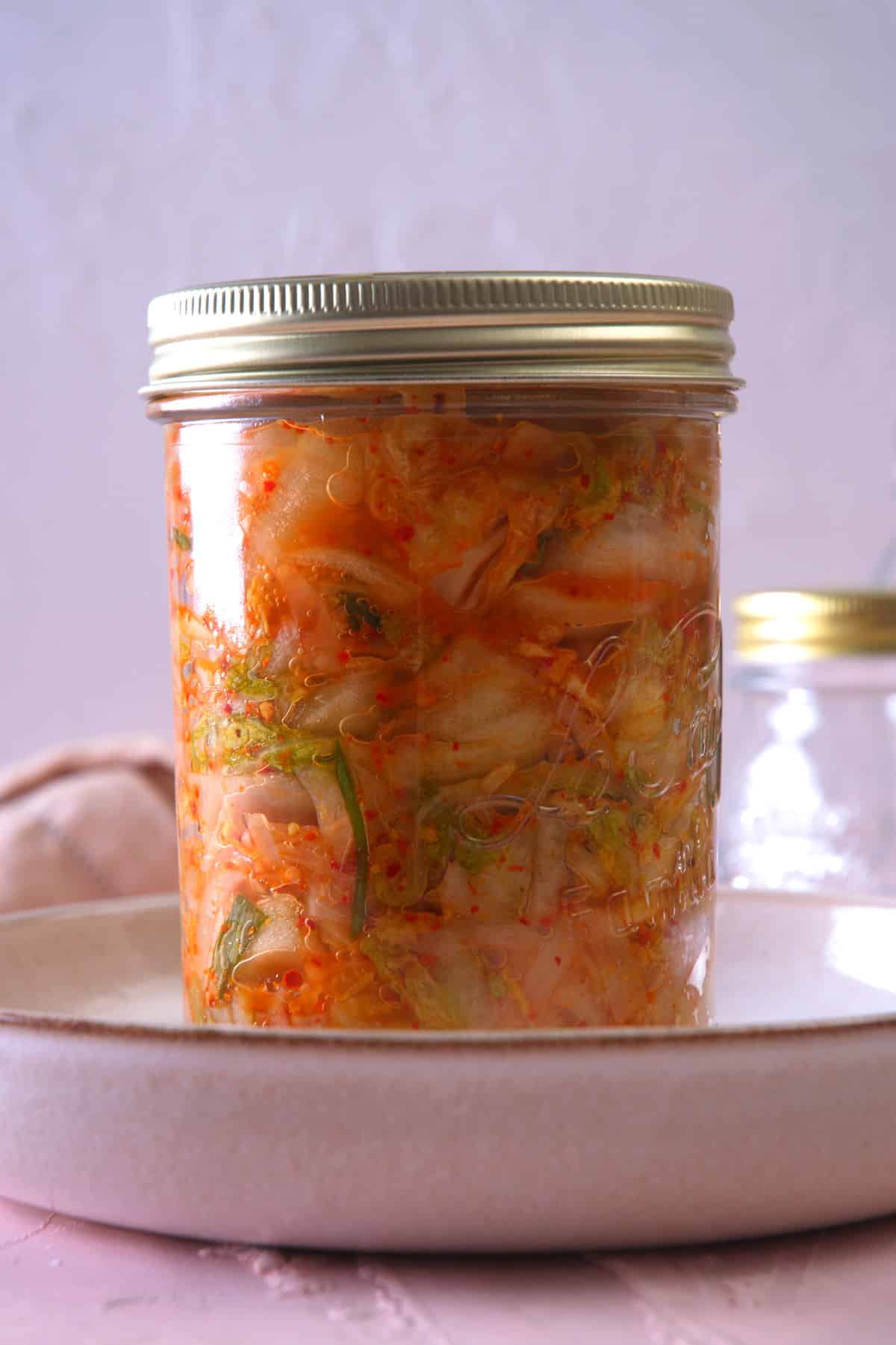 Kimchi in a sealed jar in a white dish.