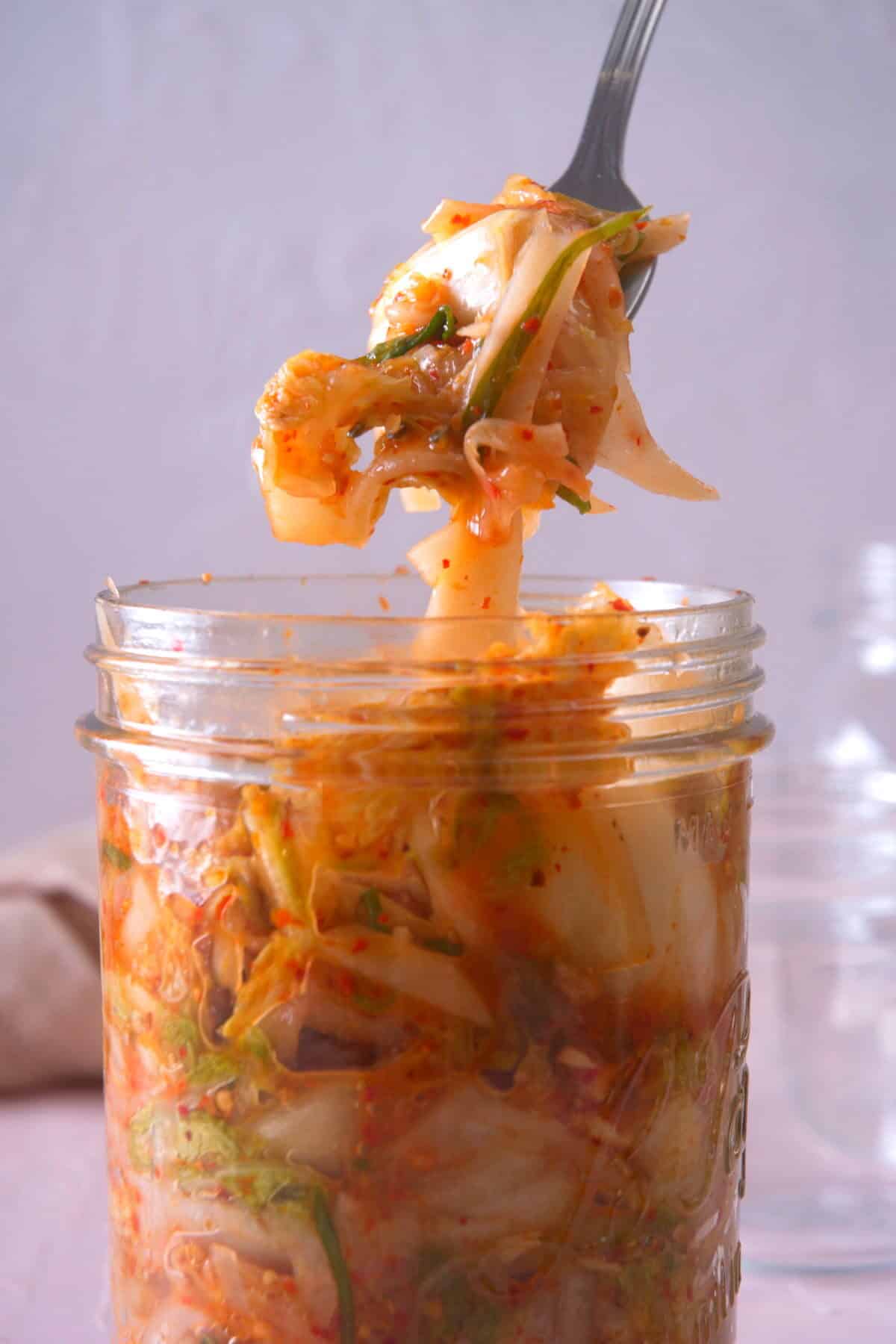 Kimchi on a fork over a jar.