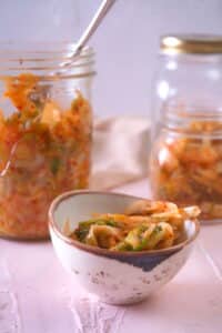 Kimchi in a small bowl with jars of kimchi in the background.