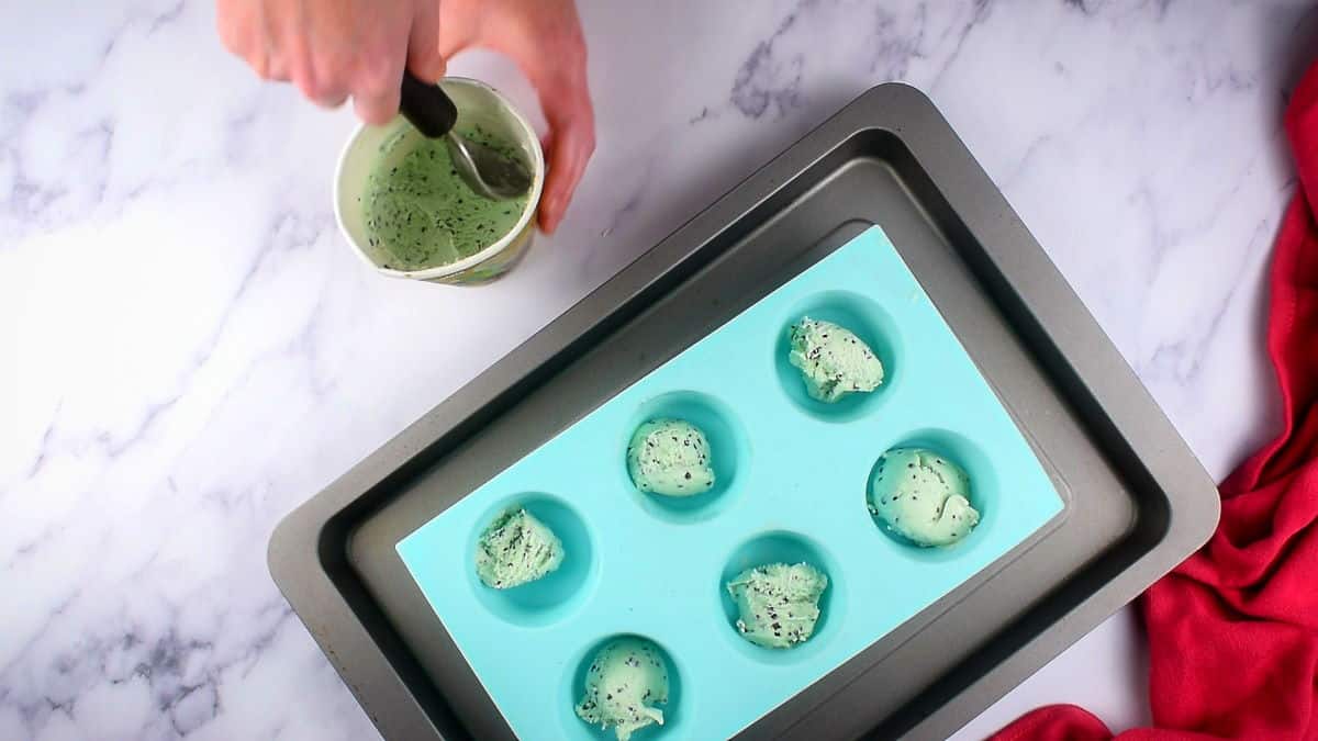 How to Make Mochi Ice Cream 2 Mint ice cream balls in a muffin tray with a small tub of ice cream and a scoop on the side, marble background.