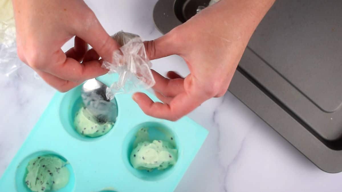 How to Make Mochi Ice Cream Step 7-4 Hands tying up mochi ice cream ball in plastic wrap.