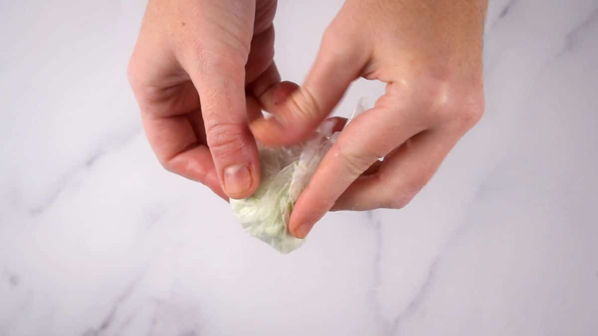 How to Make Mochi Ice Cream Step 8 Hands removing mochi ice cream ball from plastic wrap.