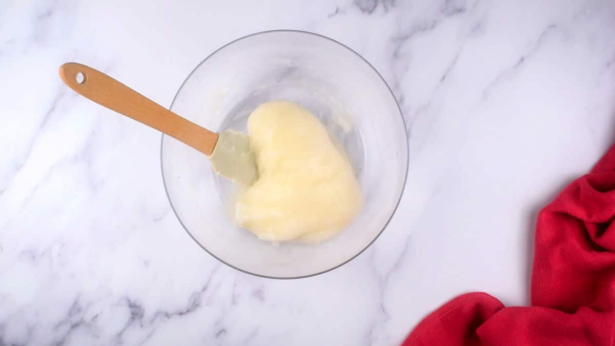 How to Make Mochi Ice Cream Step 4-6 Small glass bowl with sticky mochi dough and a spatula on marble background.
