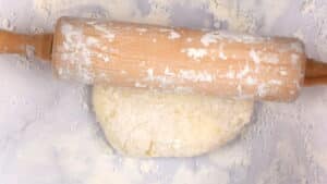 Rolling pin on mochi dough ball on floured surface.