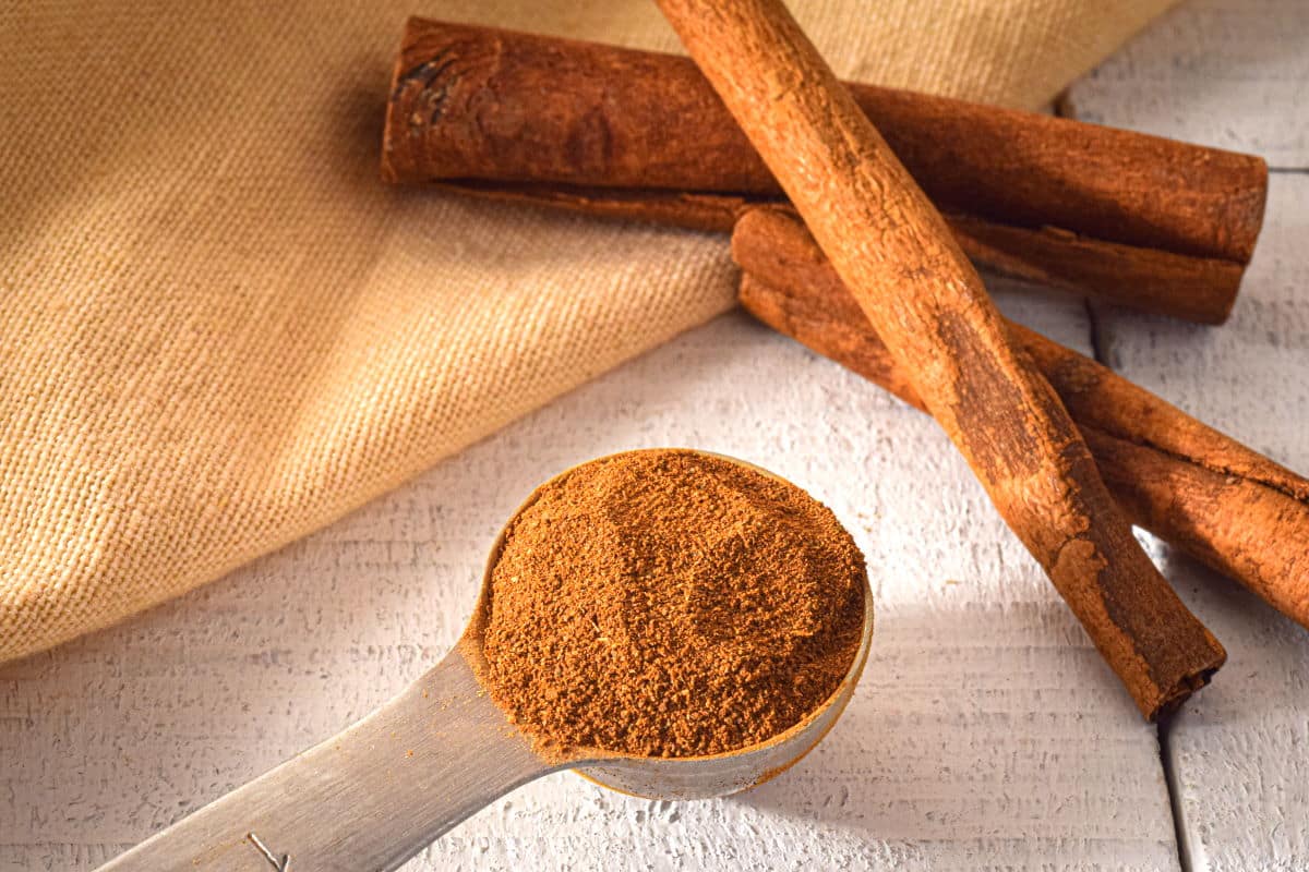 Ground cinnamon and cinnamon sticks on white, wooden background.
