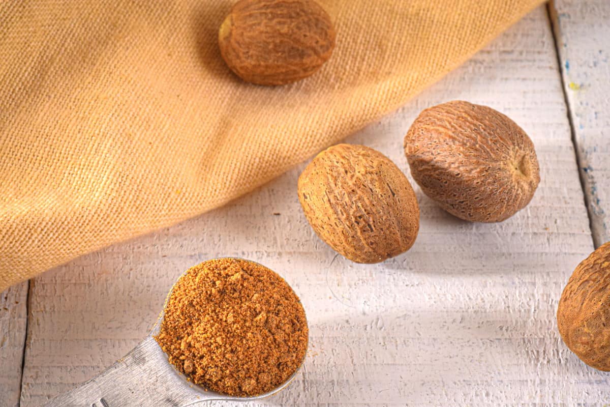 Ground and whole nutmeg on white, wooden background.