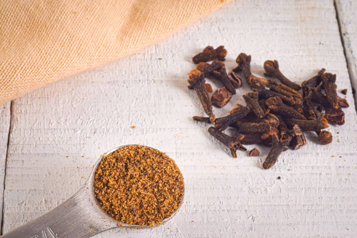 Ground and whole cloves on white, wooden background.