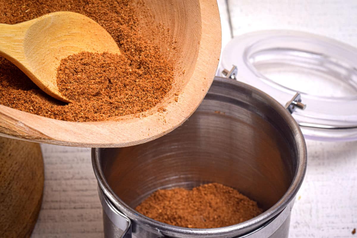 Pumpkin pie spice mix in wooden bowl with wooden spoon and a storage container.