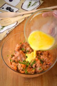 Sausage roll filling in small bowl with beaten egg.