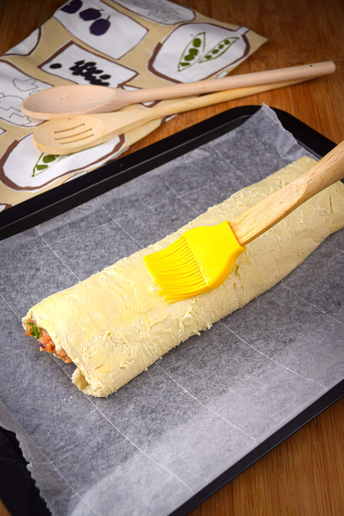 Unbaked sausage roll and pastry brush on baking sheet.