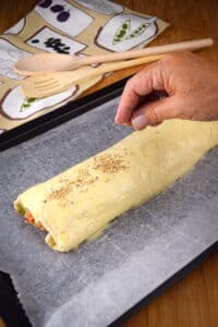 Unbaked sausage roll on baking sheet.