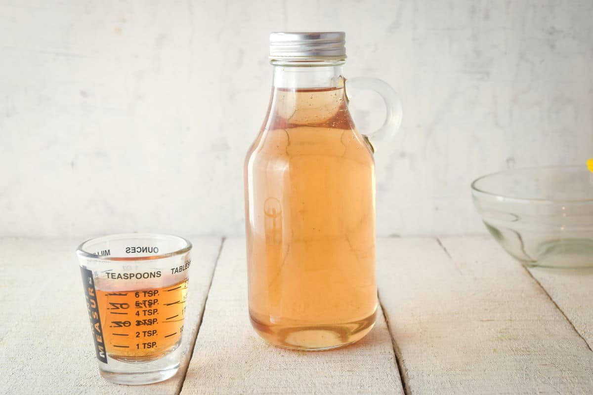 A glass bottle of simple syrup, and a small measuring glass on the side.