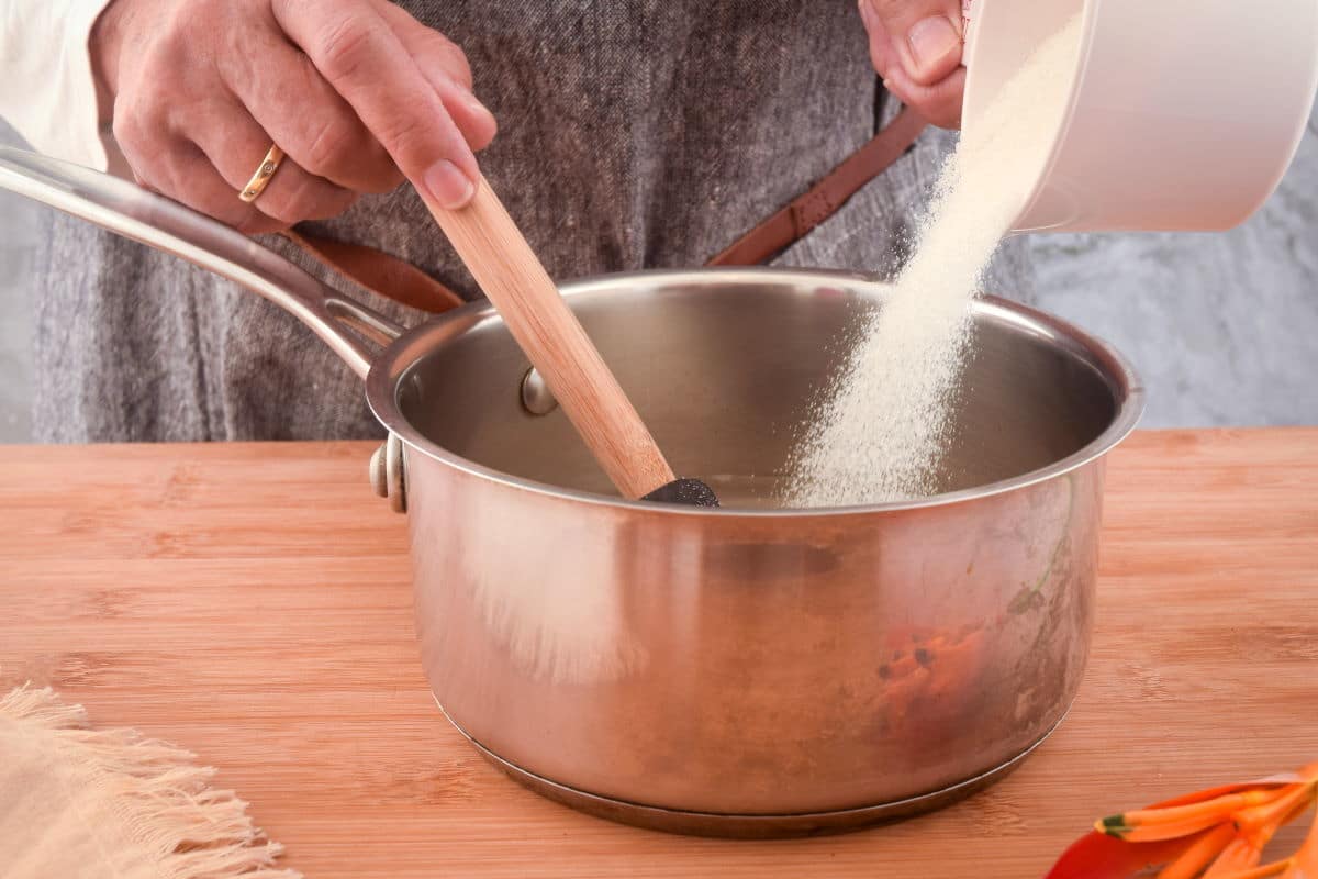 How to Make Simple Syrup Step 3 Woman's hand pouring sugar into a pot and mixing with water.
