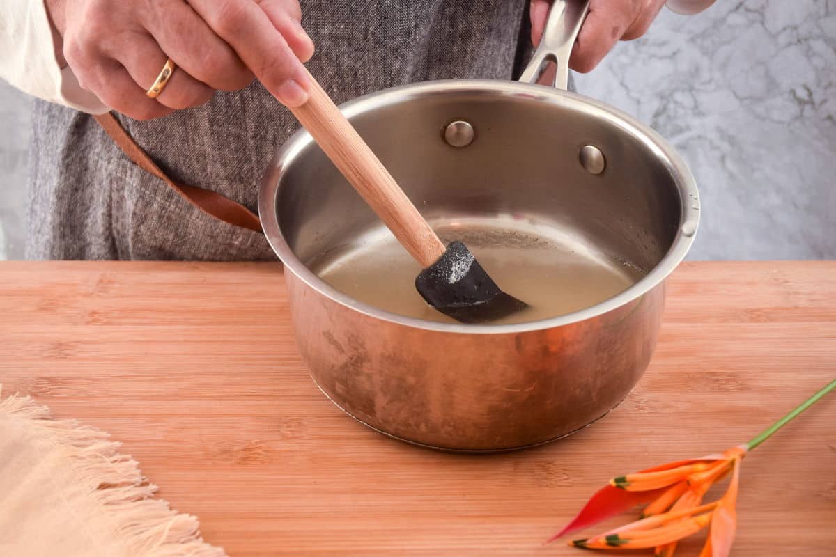 How to Make Simple Syrup Step 4 Woman's hand mixing a sugar and water mixture in a pot.