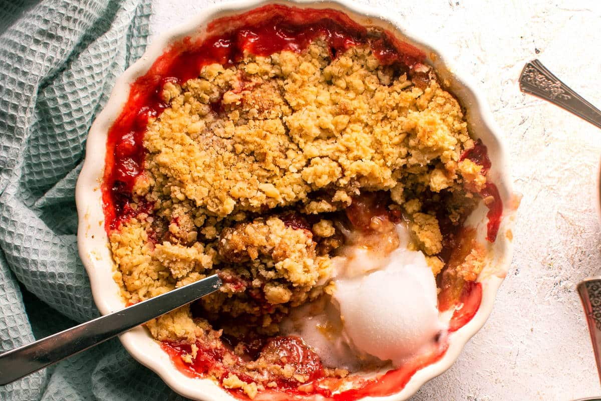 Strawberry crumble in white tart dish with a light blue kitchen towel on the side.