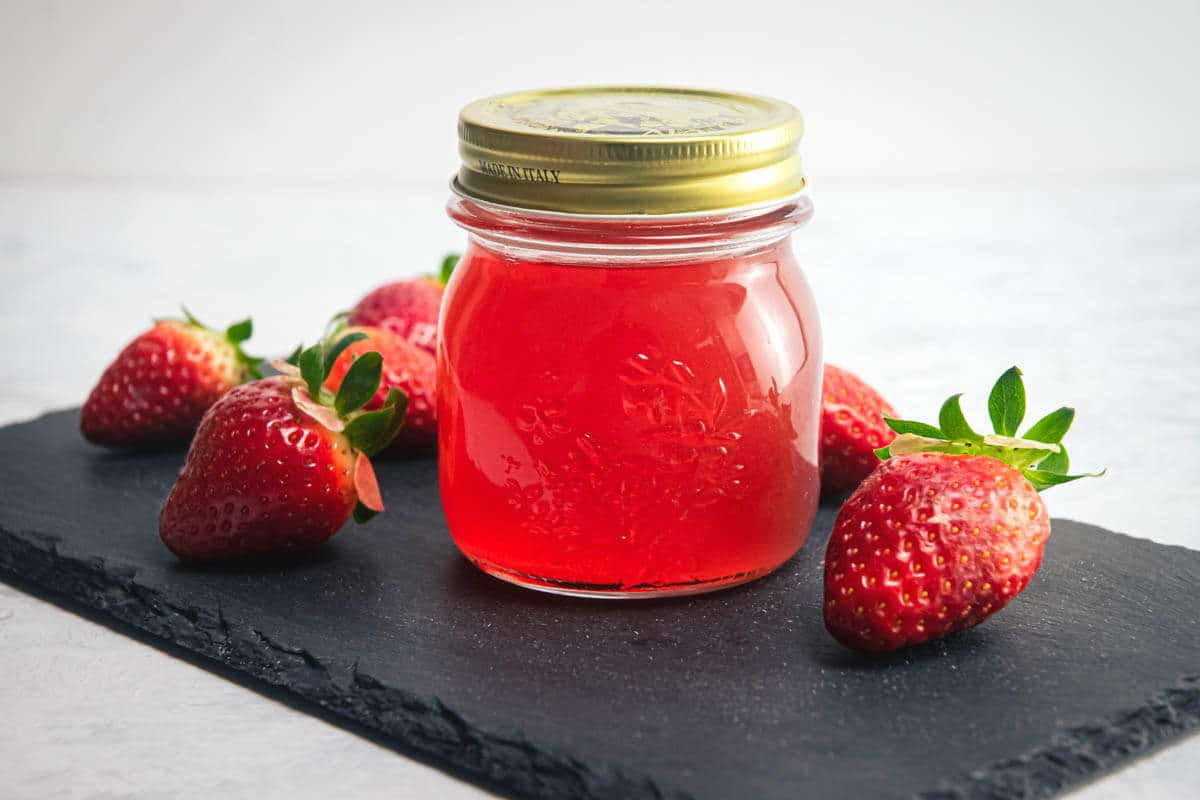 Strawberry liqueur in a jar, fresh strawberries on the side.