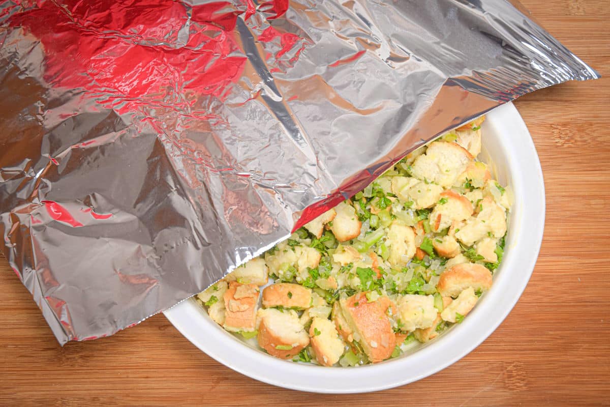 Raw stuffing mix in a white bowl with foil on top.