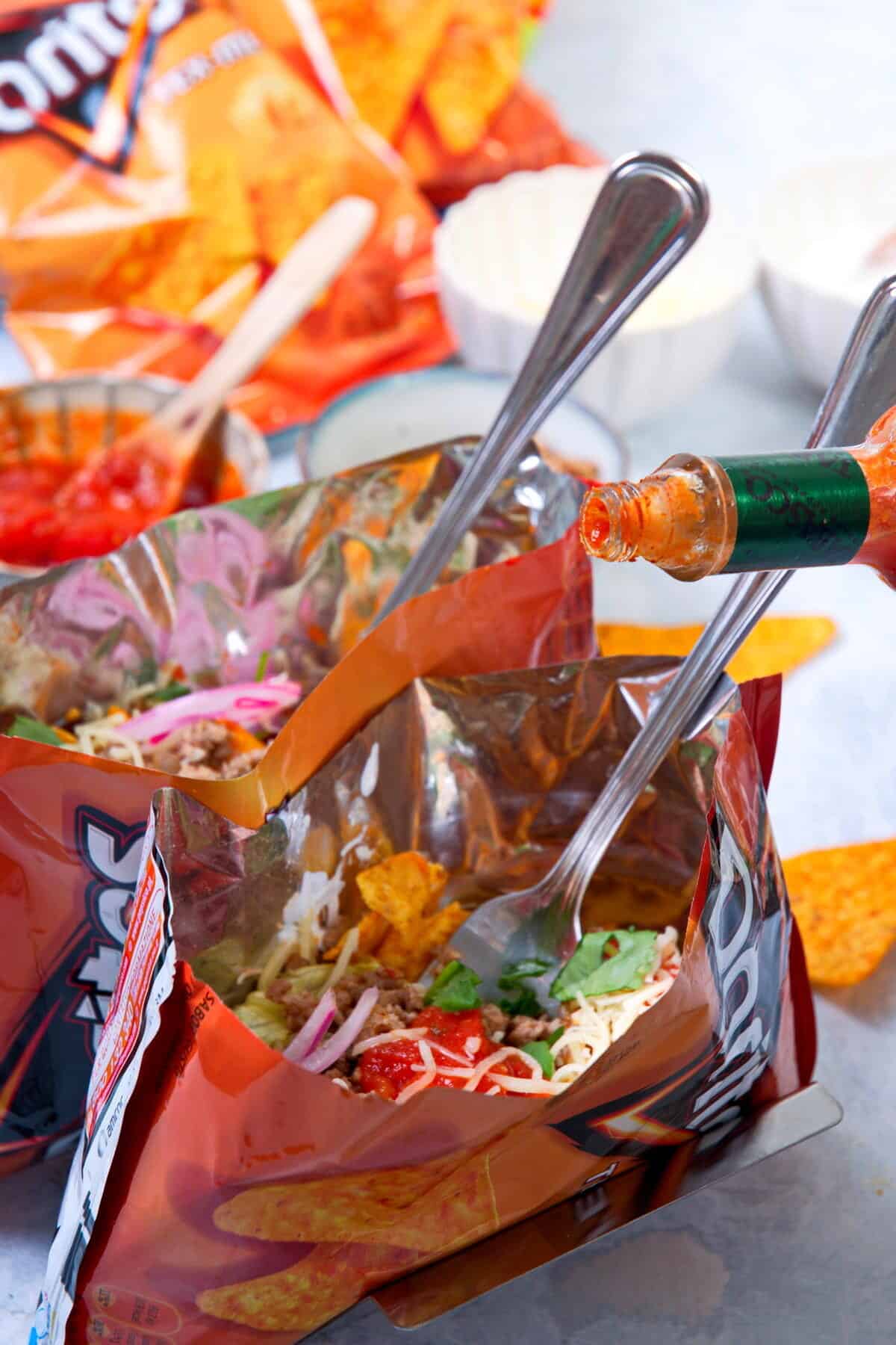 Open Dorito bags with taco filling and a bottle of hot sauce.