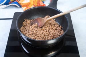 Cooked ground beef in a pan with a wooden spoon.