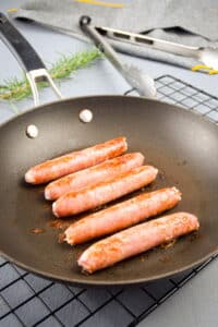 Golden English sausages in frying pan.