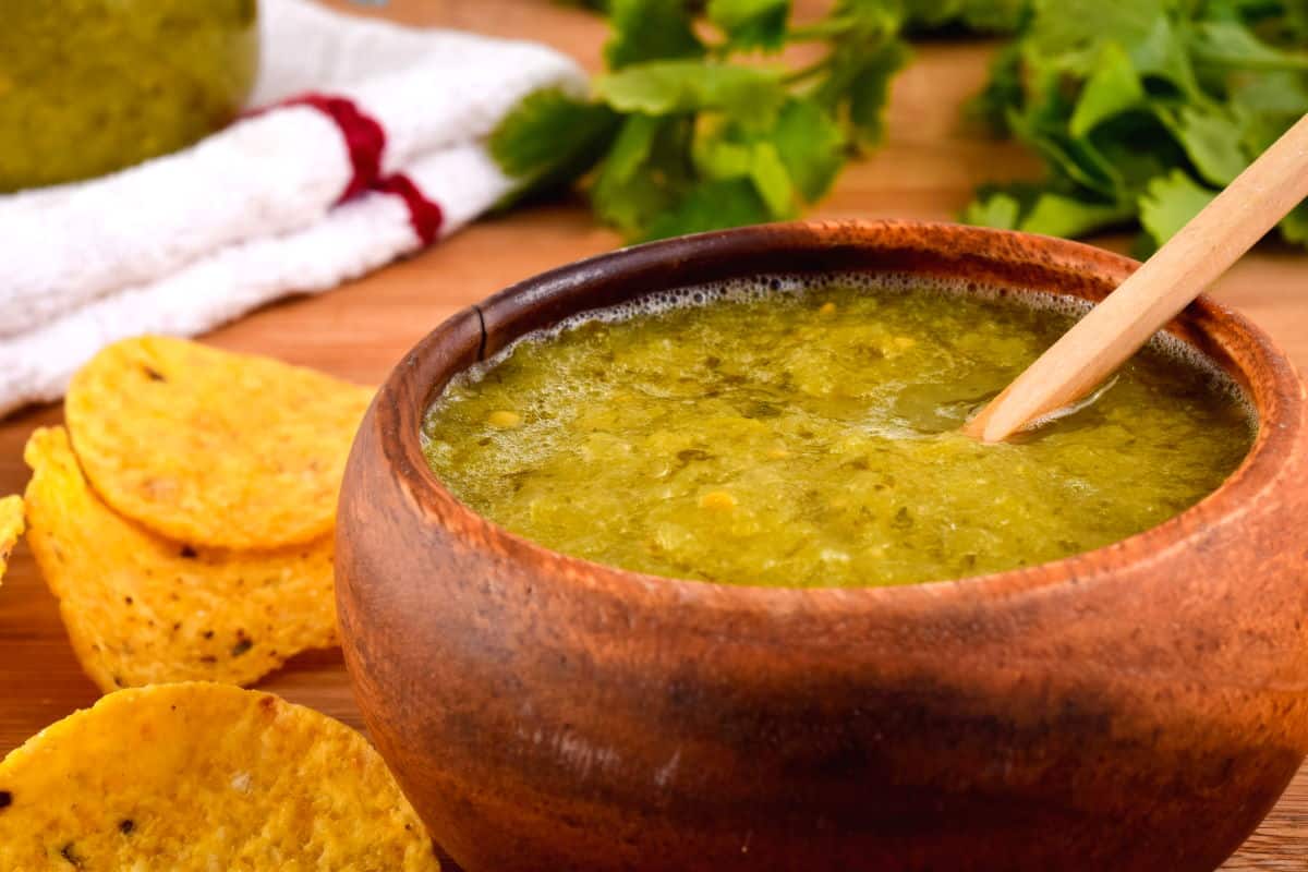 How to Make Tomatillo Salsa_13 A wooden bowl of tomatillo salsa, a jar of tomatillo salsa, cilantro and tortilla chips in the background.