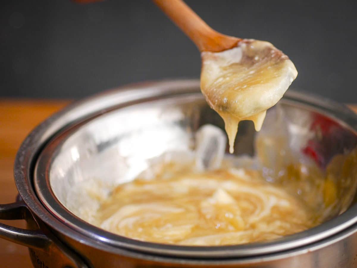 How to Make White Chocolate Ganache - Step 3 While chocolate ganache on a spoon and in a metal bowl.