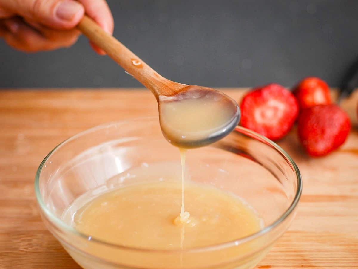 How to Make White Chocolate Ganache - Step 4 White chocolate ganache drizzling from a spoon into a clear glass bowl.