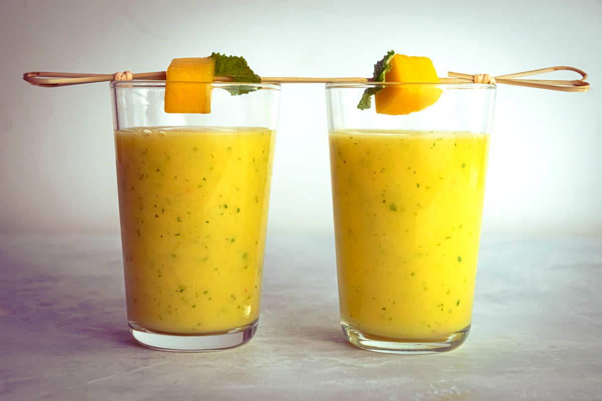 Mango pineapple smoothies in 2 glasses with mango and mint skewers.